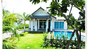 Una casa con piscina, rodeada de césped cuidado y plantas tropicales.