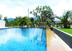 A swimming pool with clear blue water, surrounded by lush greenery and a view of distant mountains.