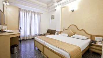 Une chambre d’hôtel avec un lit, un bureau, une chaise et une petite poubelle.