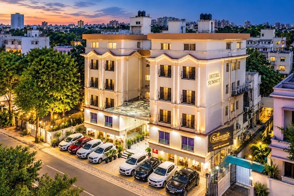 A multi-story hotel with a prominent entrance, a rooftop terrace, and a parking area with several cars. - Hotel Summit (Ahmedabad)