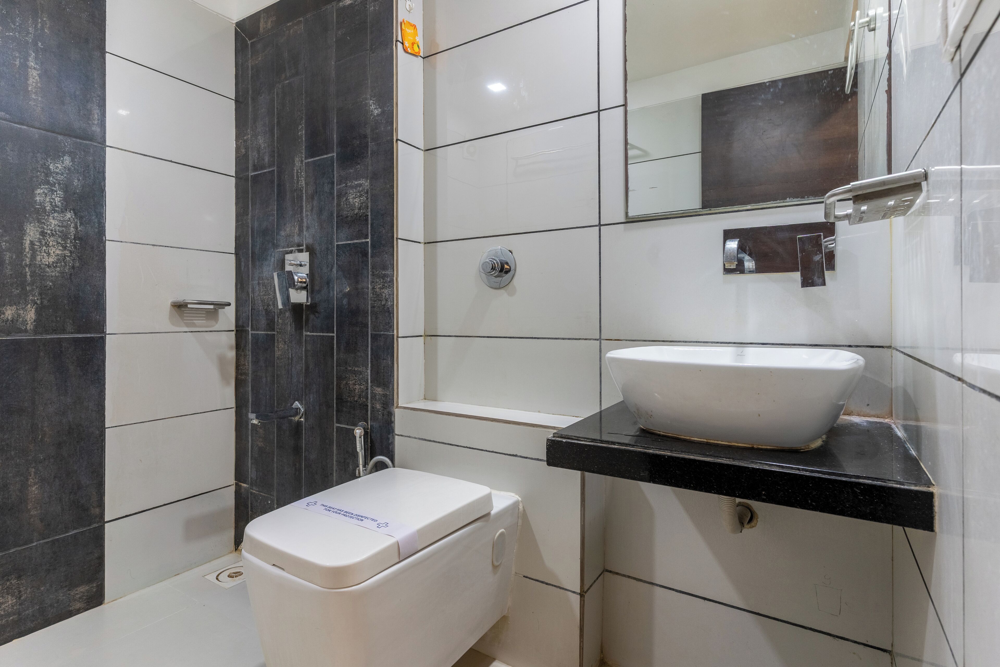 A modern bathroom with a white toilet, a black sink, and a mirror above the sink.