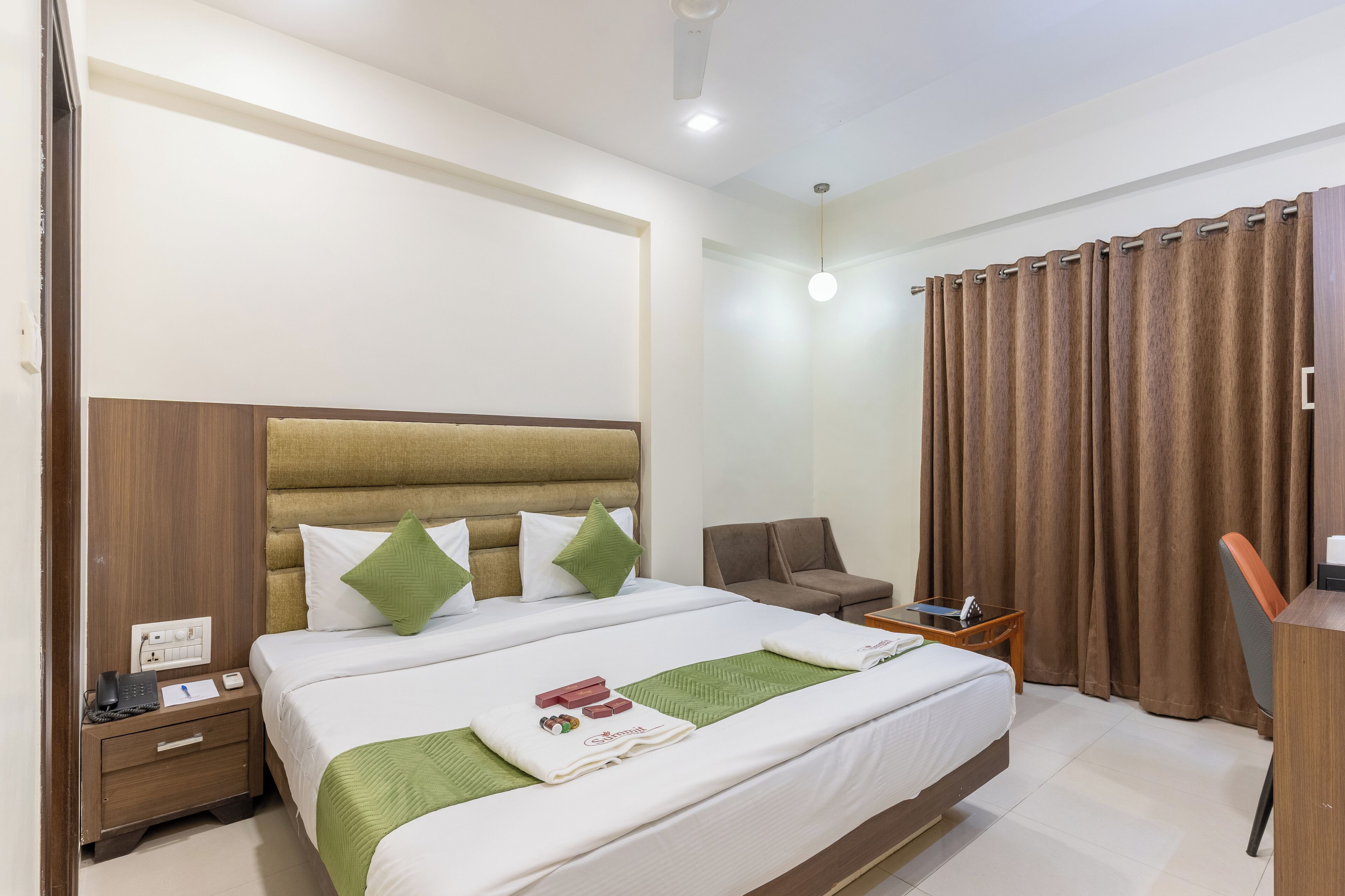 A hotel room with a large bed, a desk, a chair, and a nightstand.