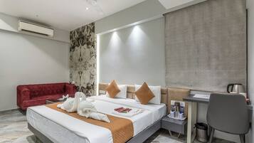 A hotel room with a bed, a red sofa, a desk, and a chair.