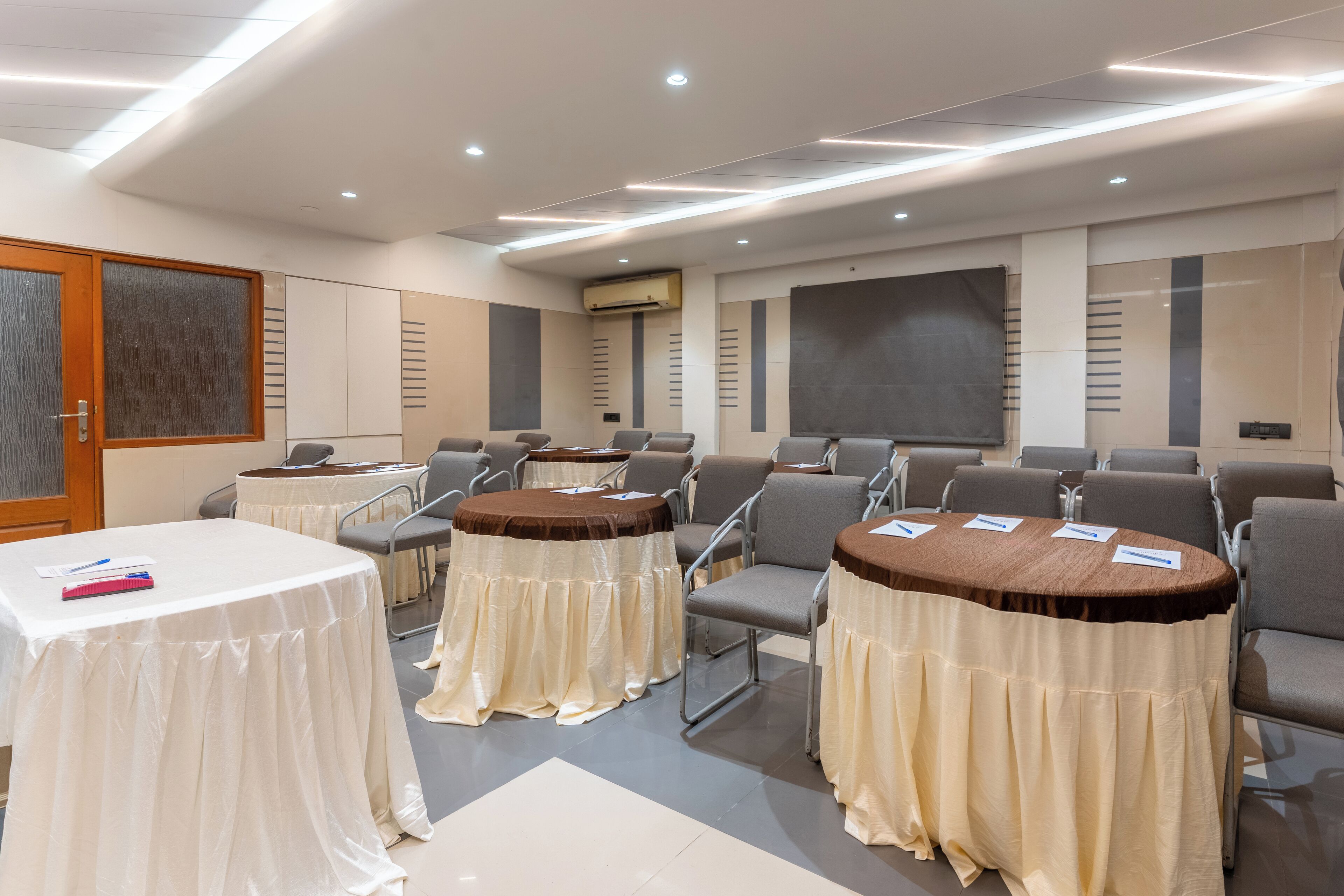 Une salle de conférence équipée de tables rondes, de chaises et d’un grand écran.
