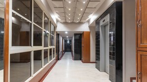 Um corredor com portas de vidro, piso de azulejos e um elevador.