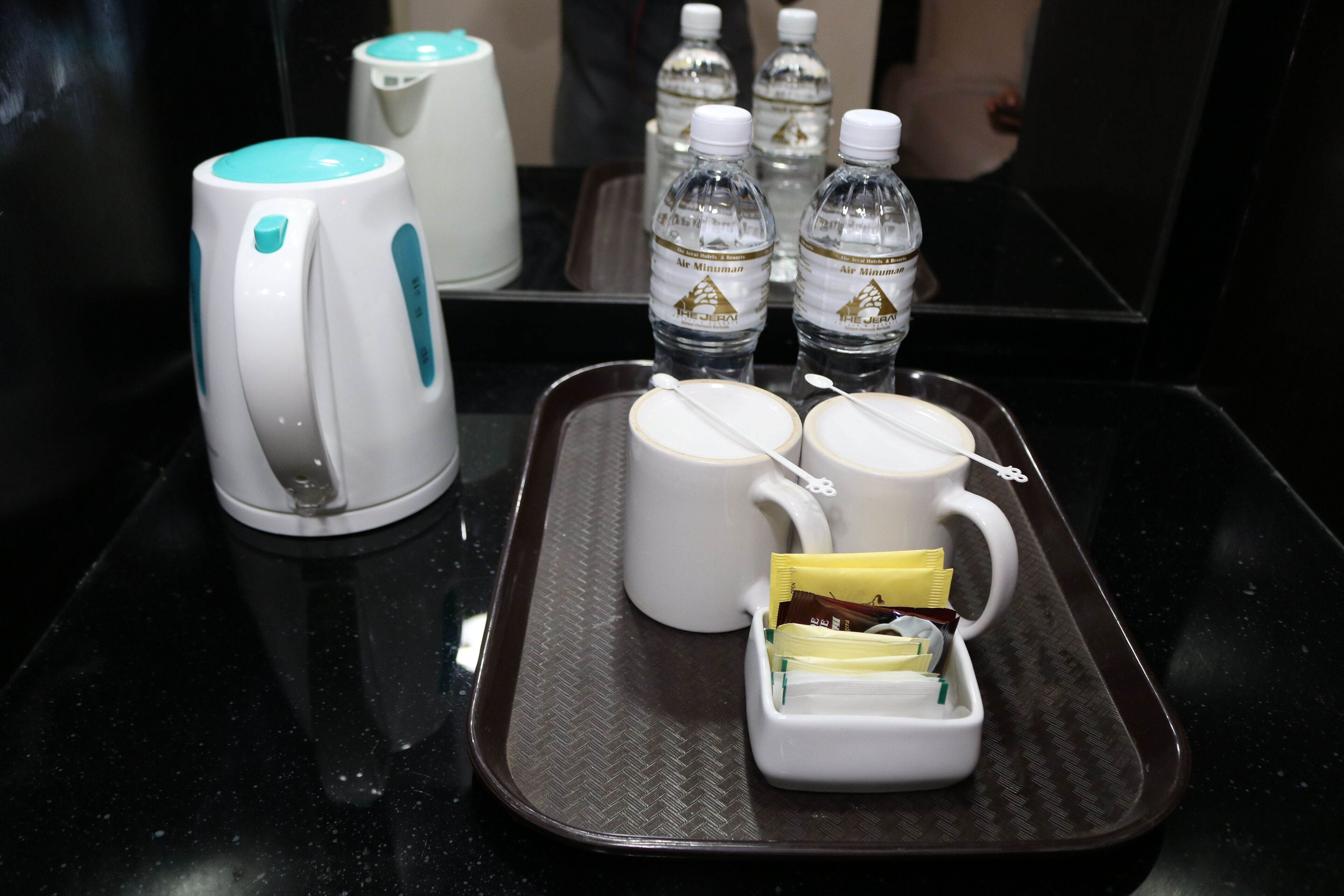 Un plateau contenant une théière, deux tasses, un petit récipient avec des ustensiles et trois bouteilles d’eau.
