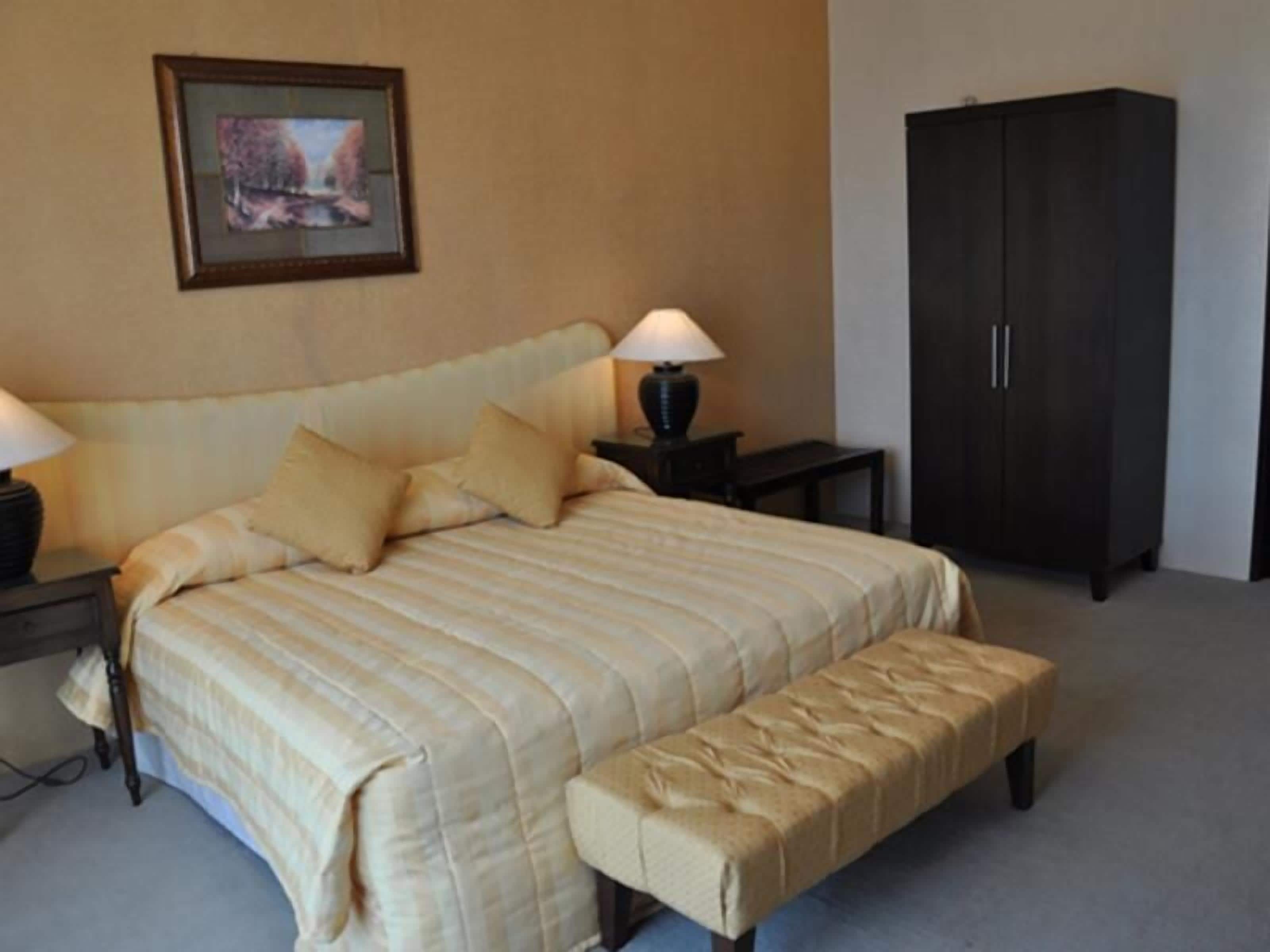 A bedroom with a large bed, two bedside tables with lamps, a dark wardrobe, and a framed picture on the wall.