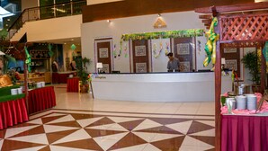 A hotel reception area with a check-in counter, a patterned floor, and a staircase in the background.