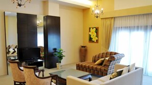 A living room with a sofa, armchairs, a coffee table, a TV, and a large window with curtains.