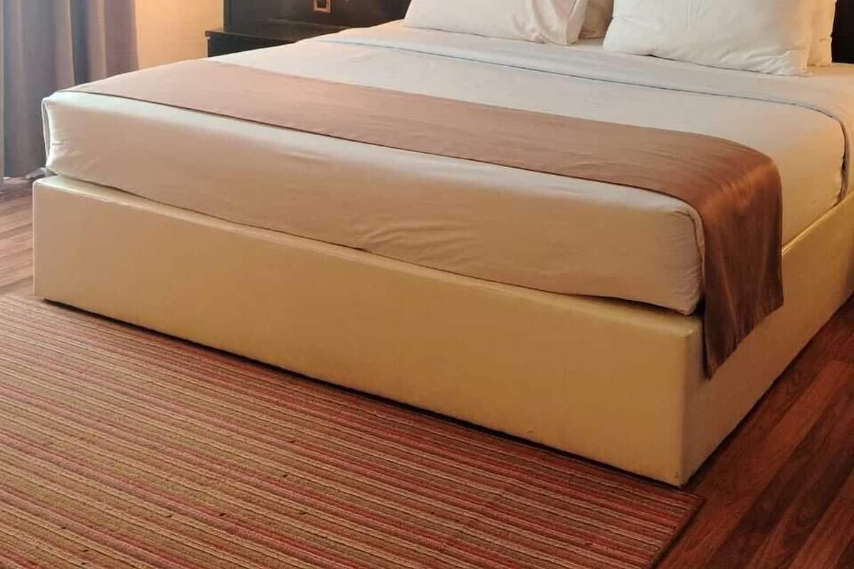 Ein Hotelzimmer mit einem großen Bett, einem dunklen Kopfteil, einem Nachttisch mit Lampe und einem Fenster mit Vorhängen.