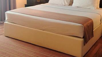 A hotel room with a large bed, a dark headboard, a nightstand with a lamp, and a window with curtains.
