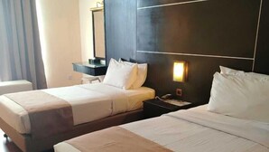 A hotel room with two beds, a nightstand, a mirror, and a window with curtains.