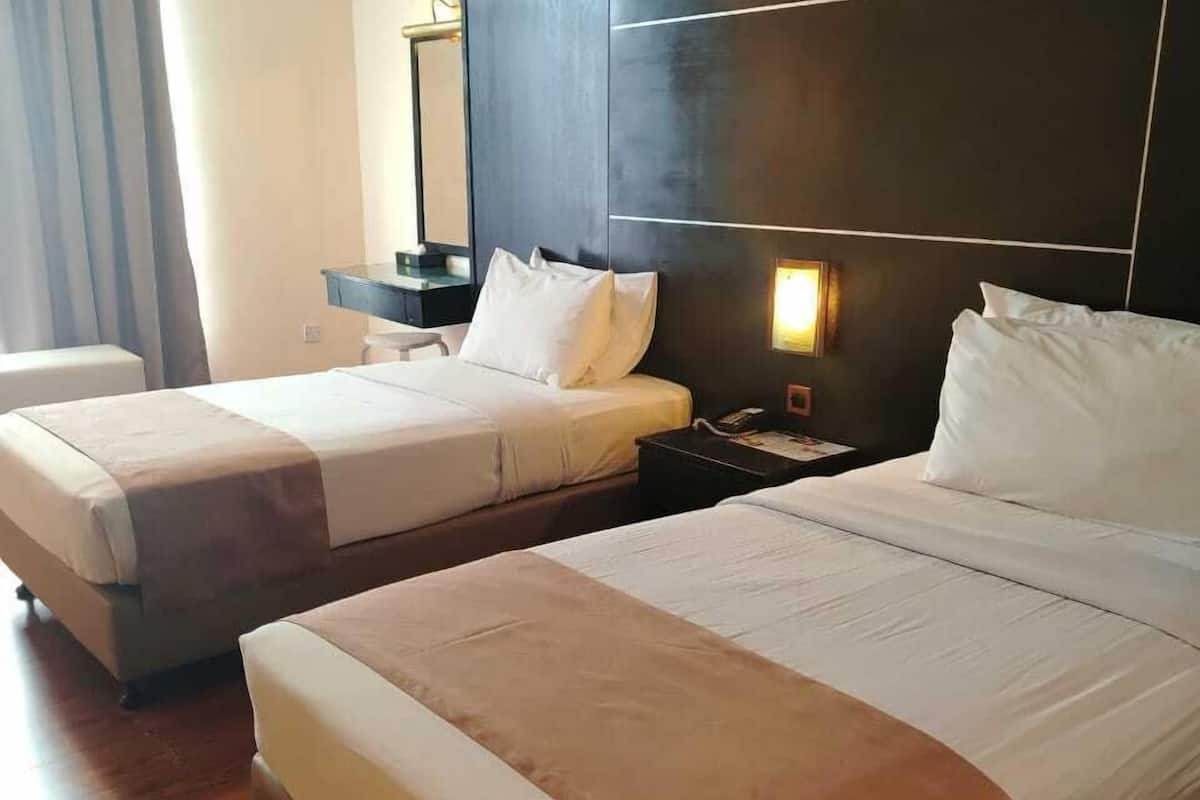 Ein Hotelzimmer mit zwei Betten, einem Nachttisch, einem Spiegel und einem Fenster mit Vorhängen.