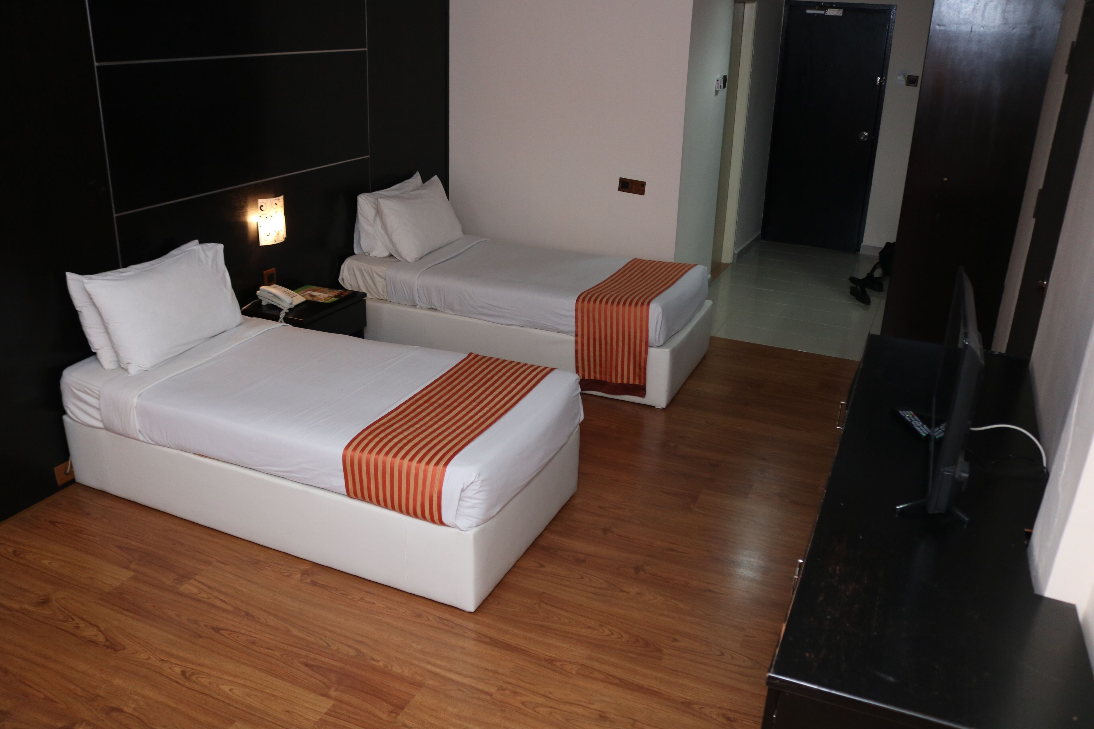 Habitación de hotel con dos camas, suelo de madera, un escritorio con computadora y televisor.