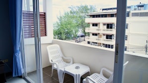 Een balkon met witte plastic stoelen en een kleine tafel, met uitzicht op een gebouw met balkons en bomen.