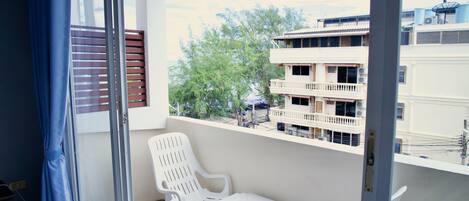 A balcony with white plastic chairs and a small table, overlooking a building with balconies and trees.