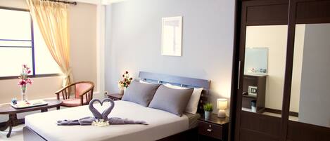A hotel room with a large bed, a bedside table with a lamp, a chair, and a desk with a vase of flowers.