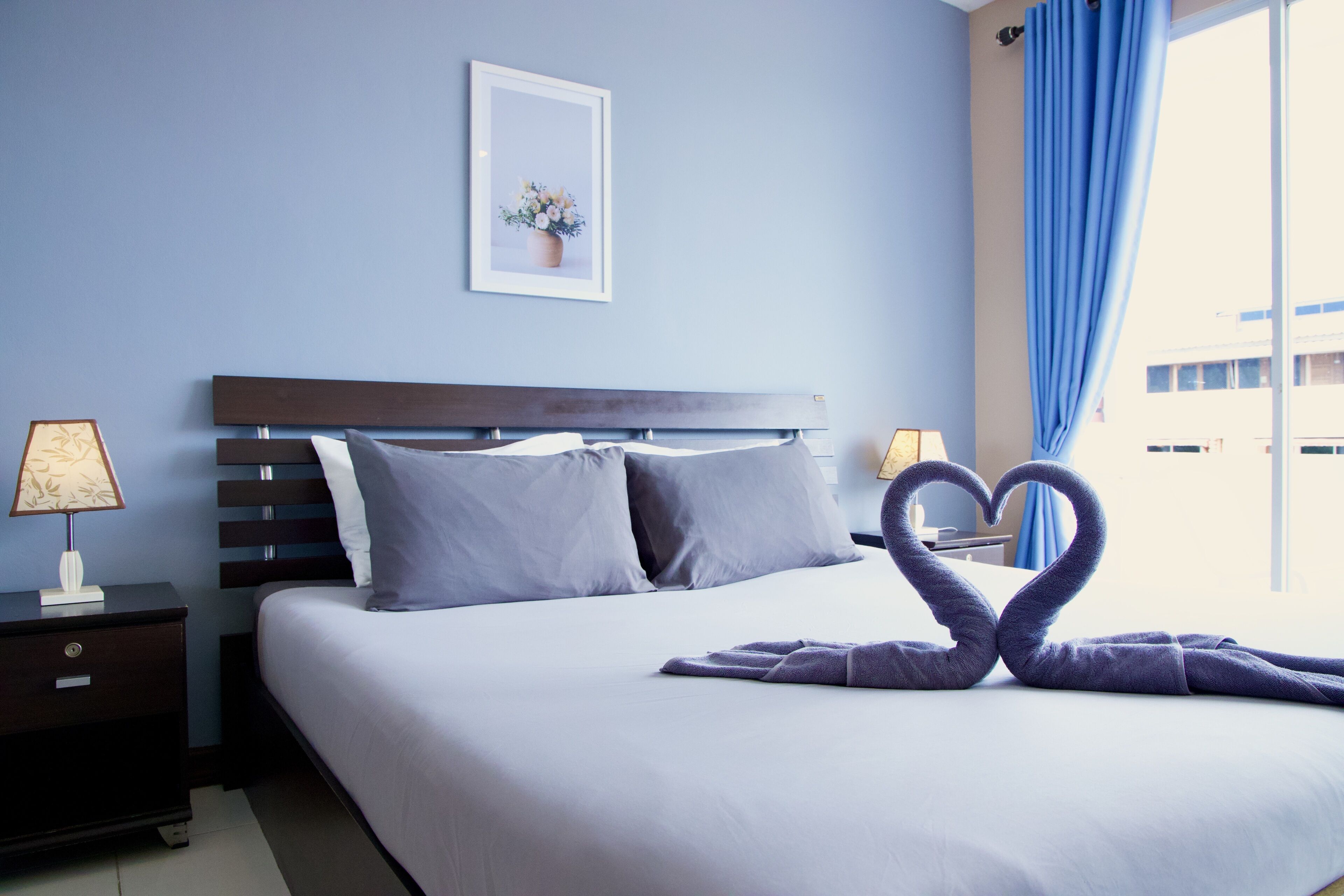 Hotelkamer met een groot bed, twee nachtkastjes, een ingelijst kunstwerk aan de muur en een raam met blauwe gordijnen.