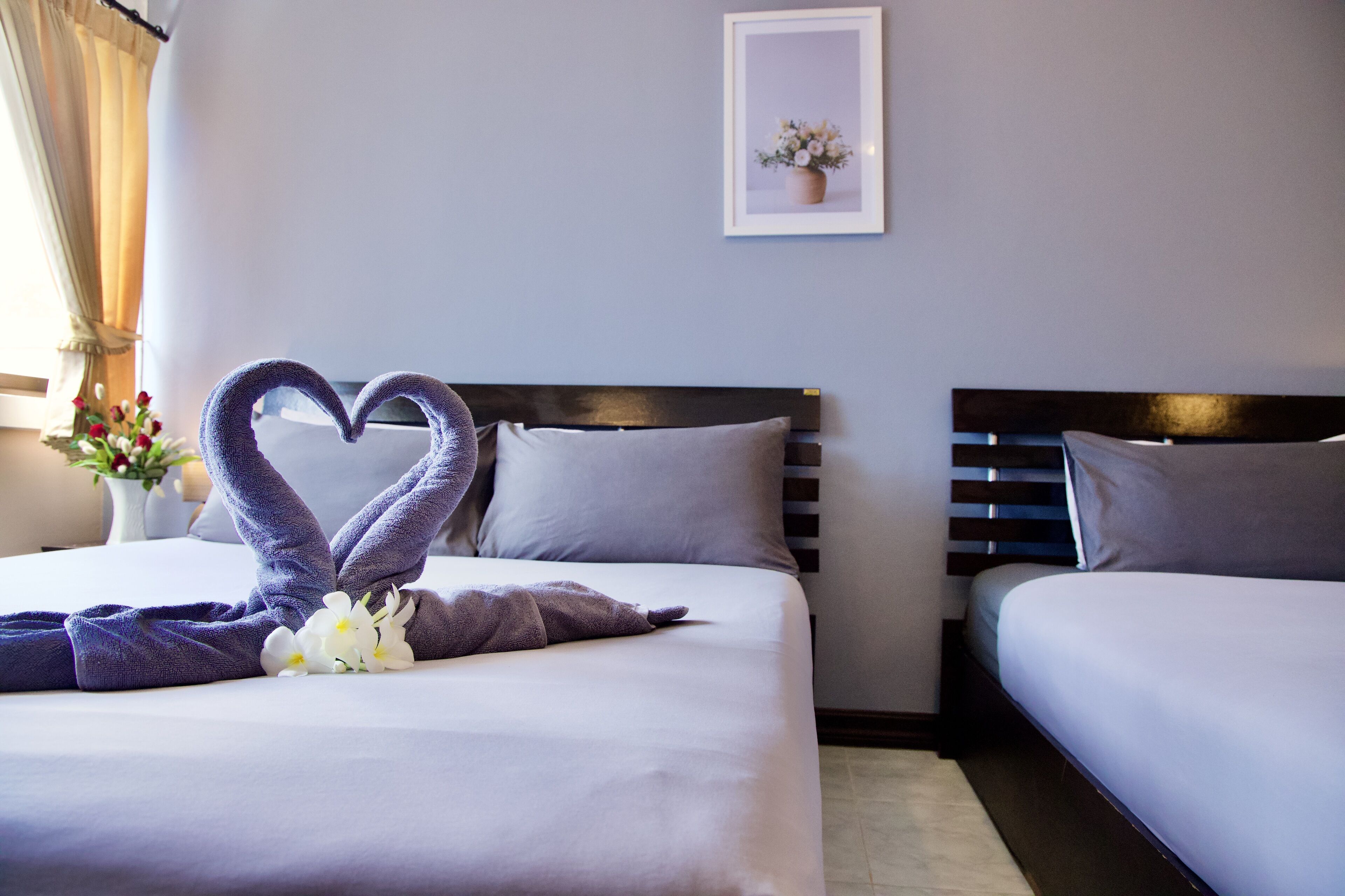 Une chambre d’hôtel avec deux lits, une décoration en forme de cœur réalisée avec des serviettes et un tableau encadré au mur.