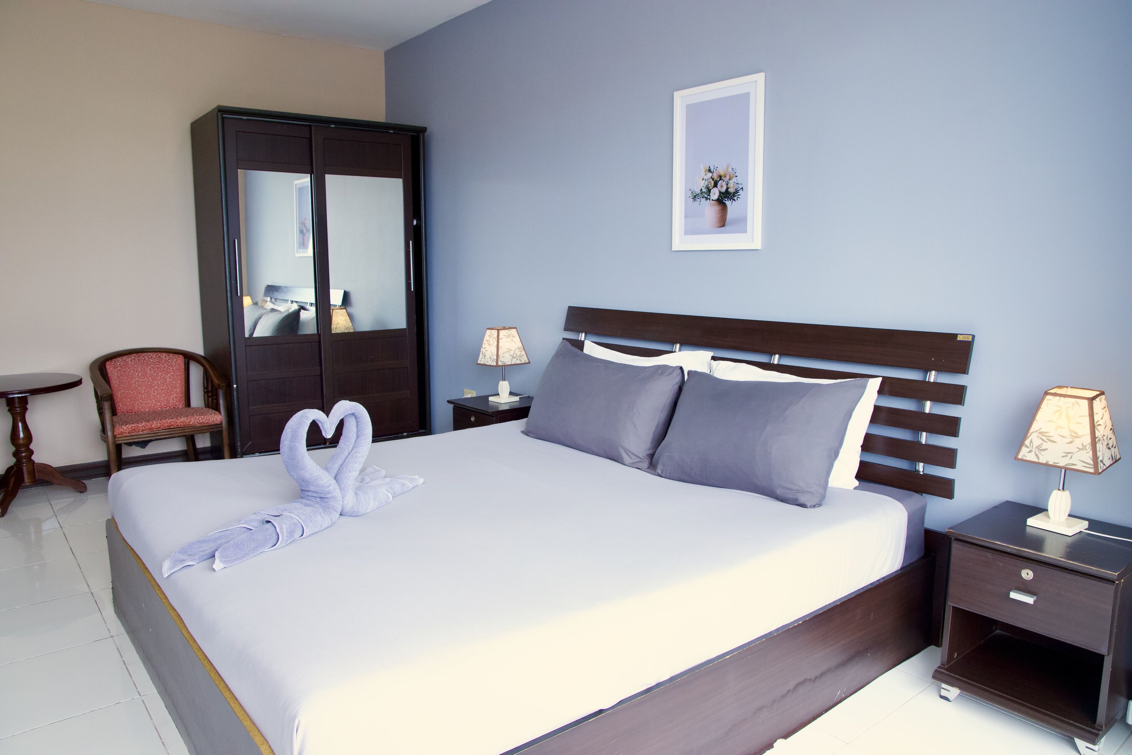 A hotel room with a large bed, two bedside tables, a chair, a wardrobe, and a framed picture on the wall.