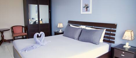 Quarto de hotel com uma cama grande, duas mesas de cabeceira, uma cadeira, um guarda-roupa e um quadro na parede.