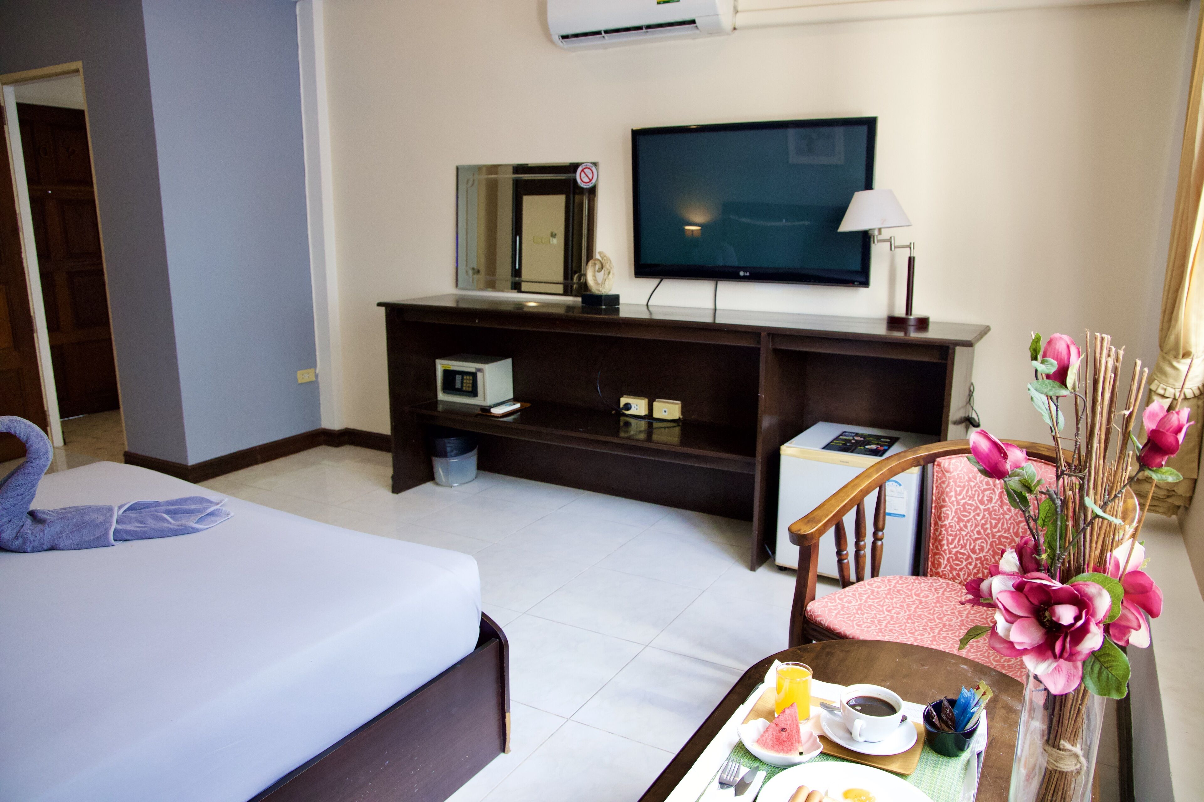 Habitación de hotel con una cama, un escritorio con computadora, televisor, una silla y una mesa con alimentos para el desayuno.