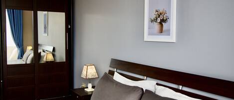 A hotel room with a large bed, a nightstand with a lamp, a mirror, a framed picture on the wall, and a wardrobe.