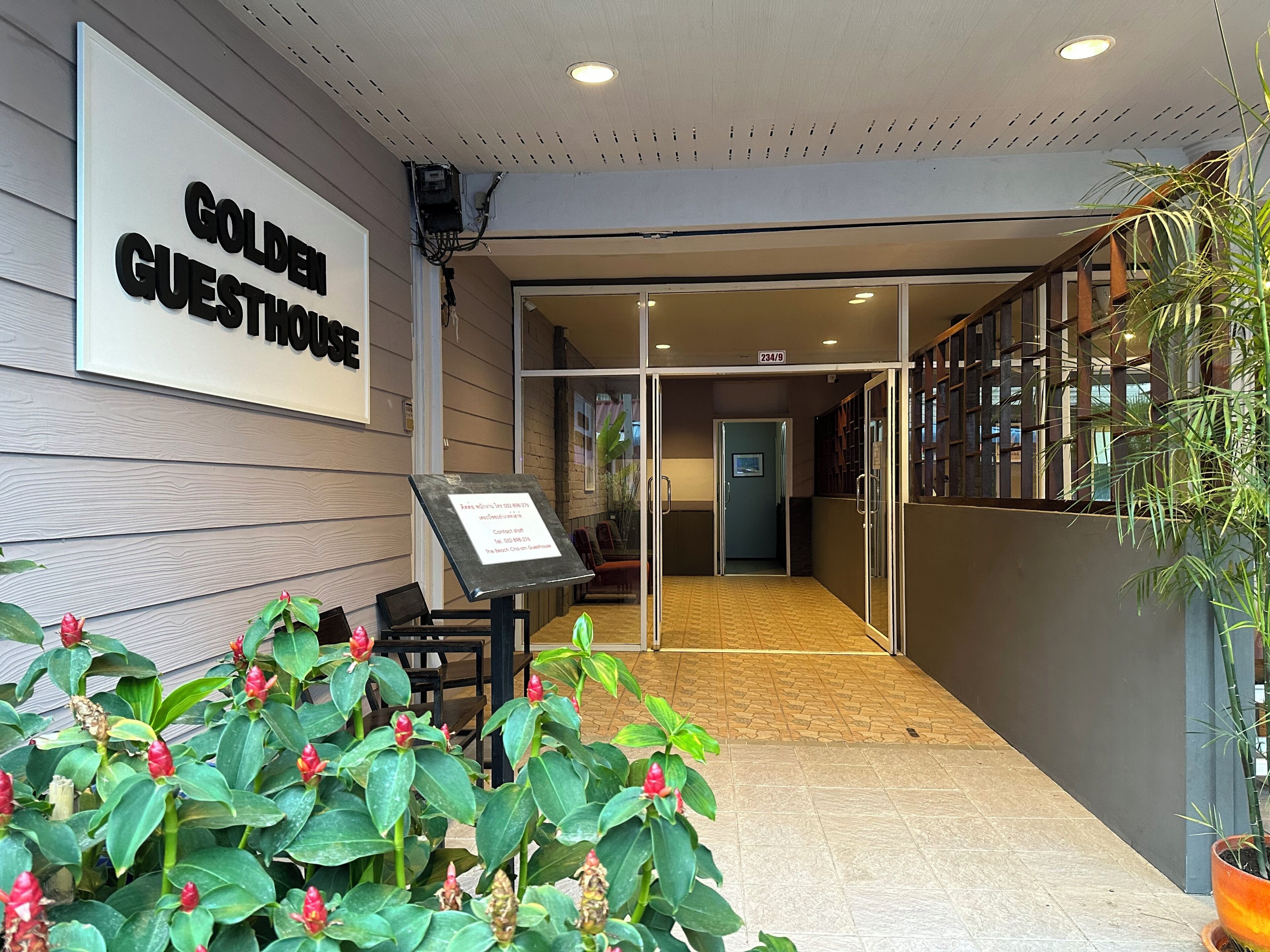 En hotelindgang med et skilt der siger 'GOLDEN GUESTHOUSE', et receptionsskrank og en potteplante.