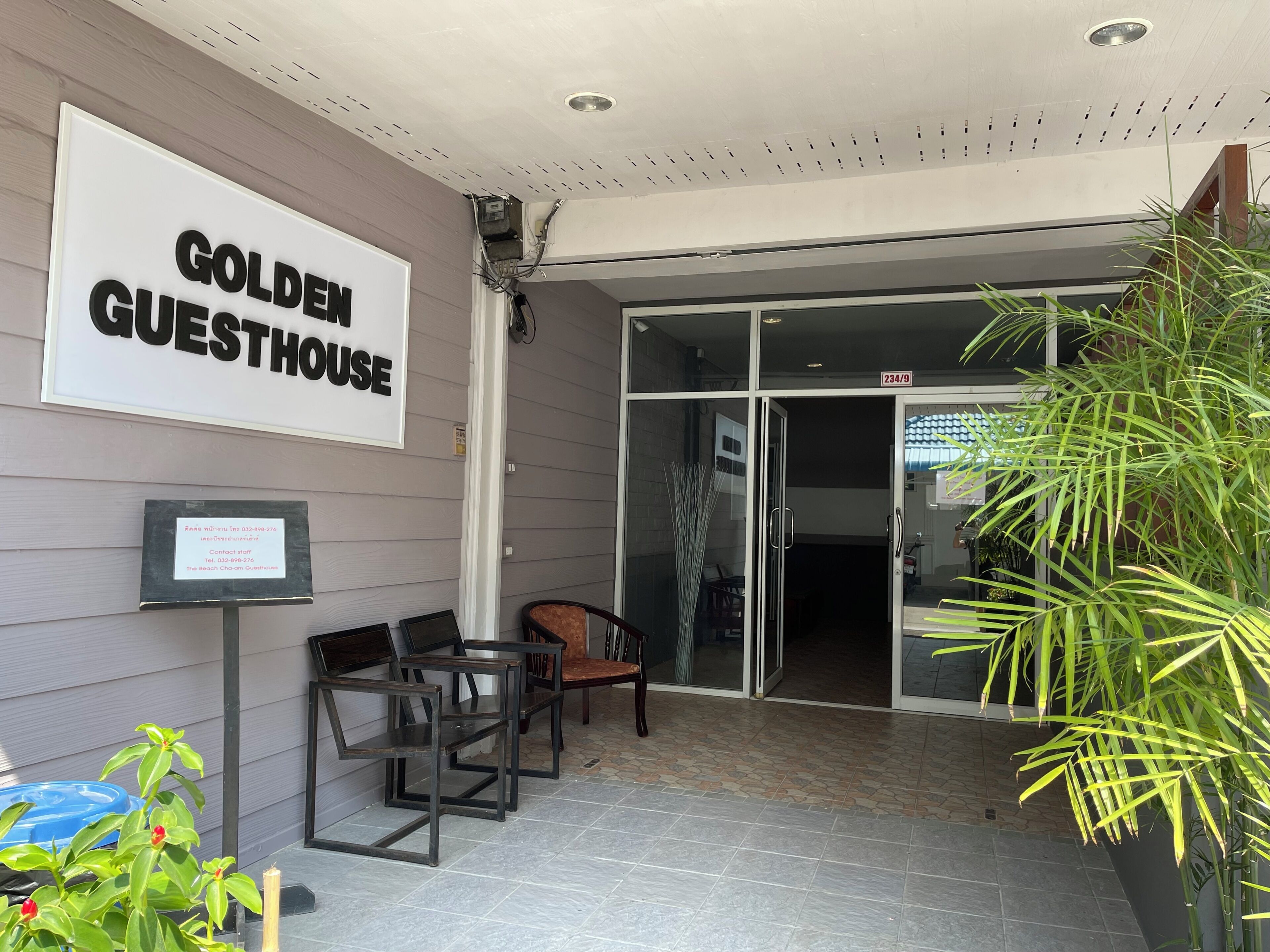 Entrada de un hotel con un letrero que dice 'GOLDEN GUESTHOUSE', una recepción y un área de descanso con sillas.