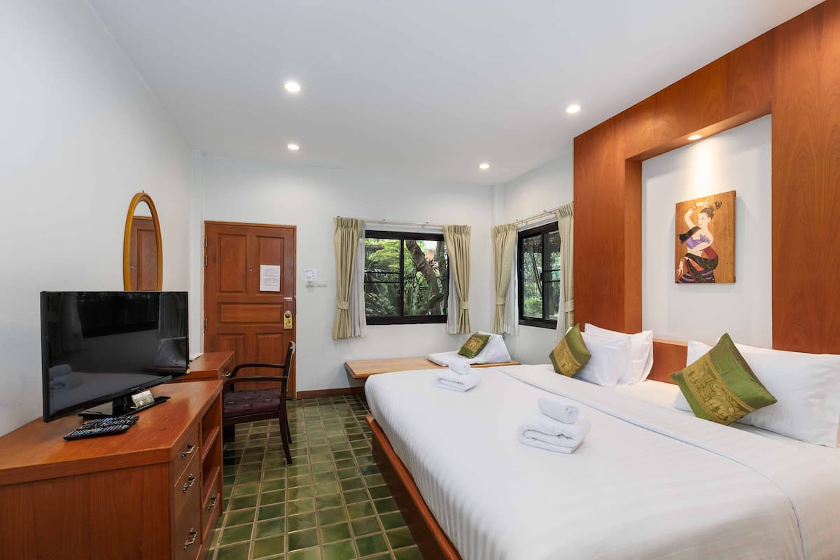 A hotel room with a bed, a desk with a TV, a chair, and a window with curtains.