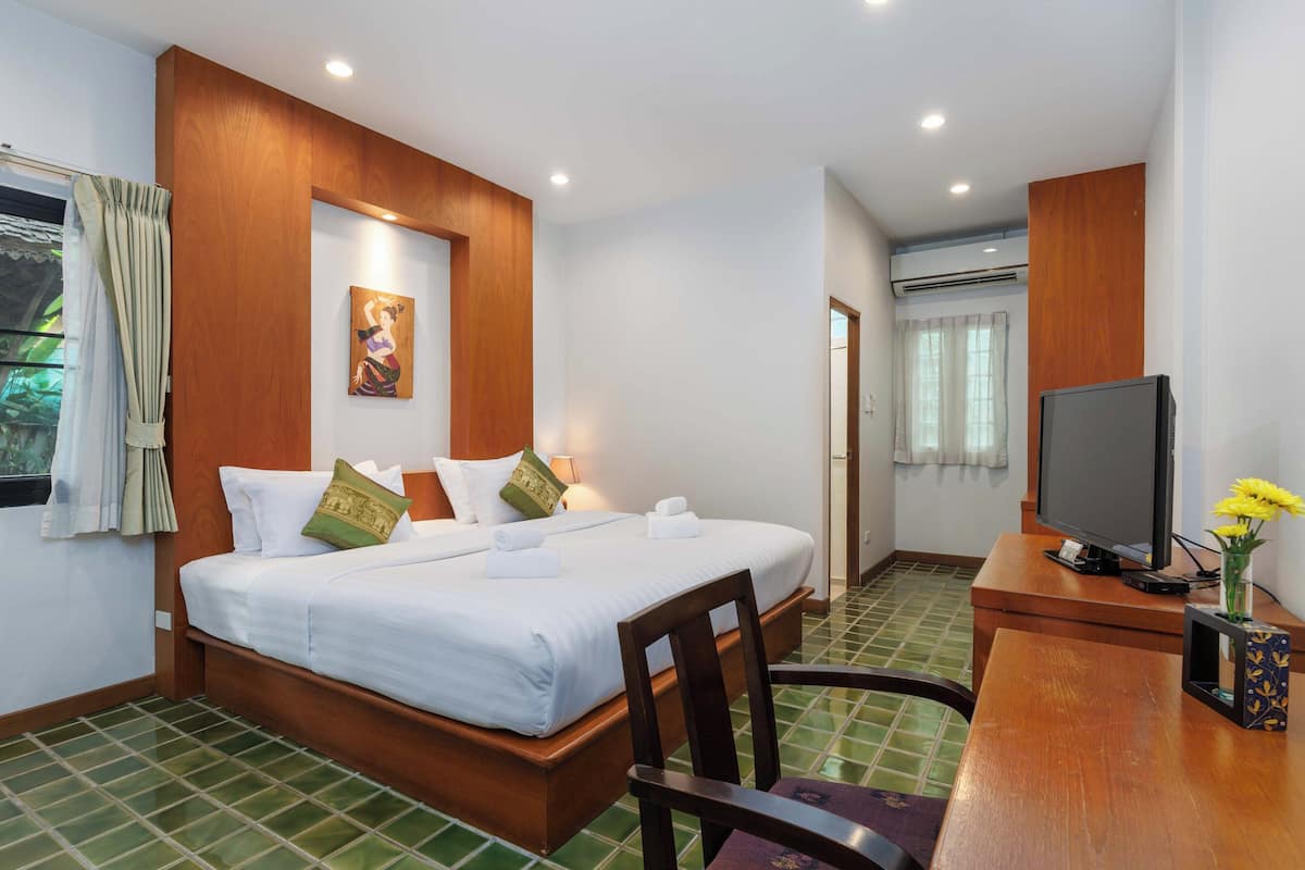 A hotel room with a bed, a desk with a TV, and a window with curtains.