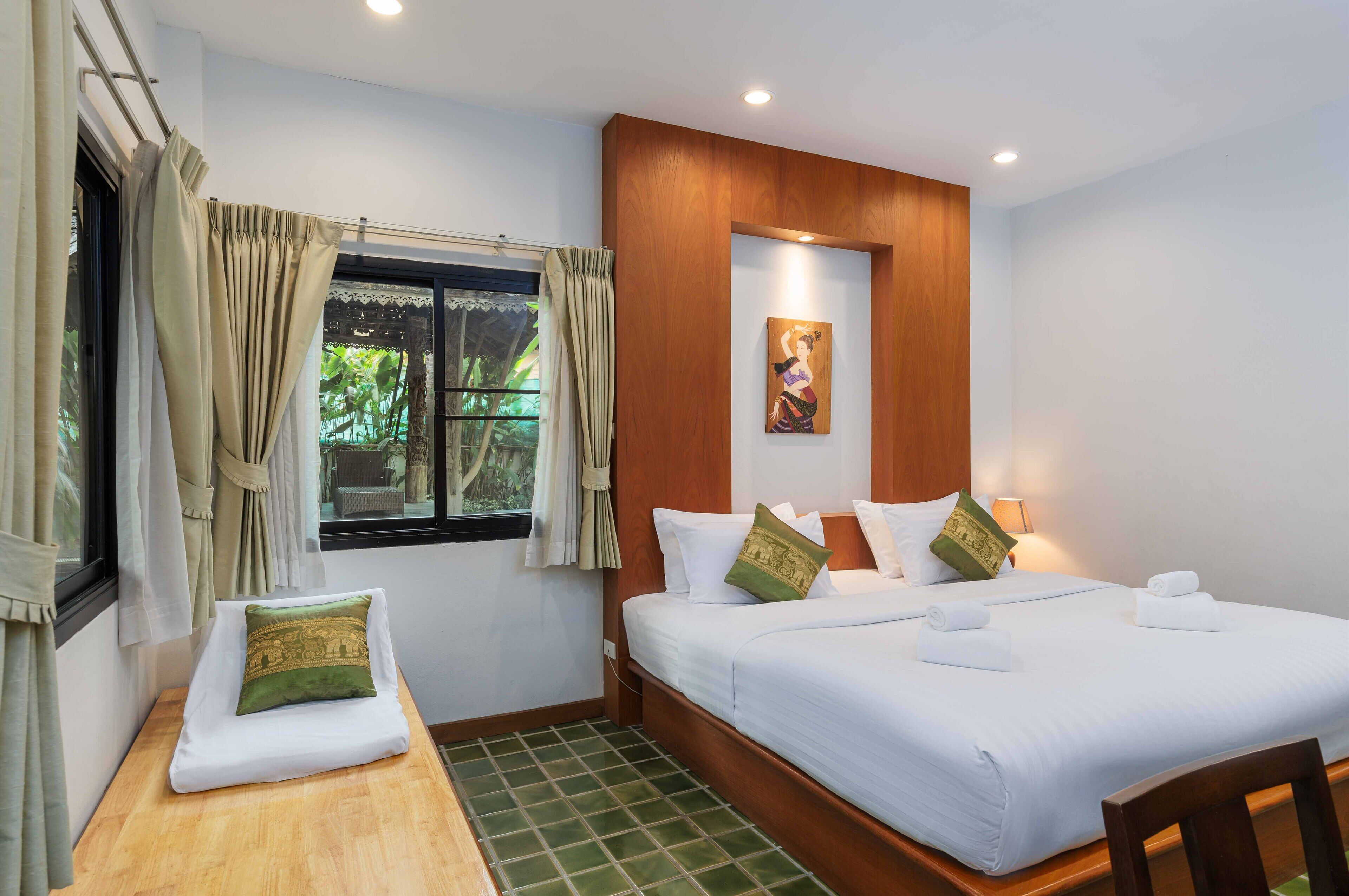 Habitación de hotel con cama, una mesita, ventana con cortinas, un cuadro en la pared y cabecera de madera.