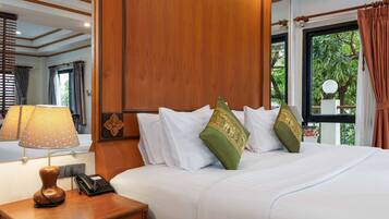 Habitación de hotel con una cama grande, una mesita de noche de madera con lámpara y teléfono, y un ventanal con cortinas.