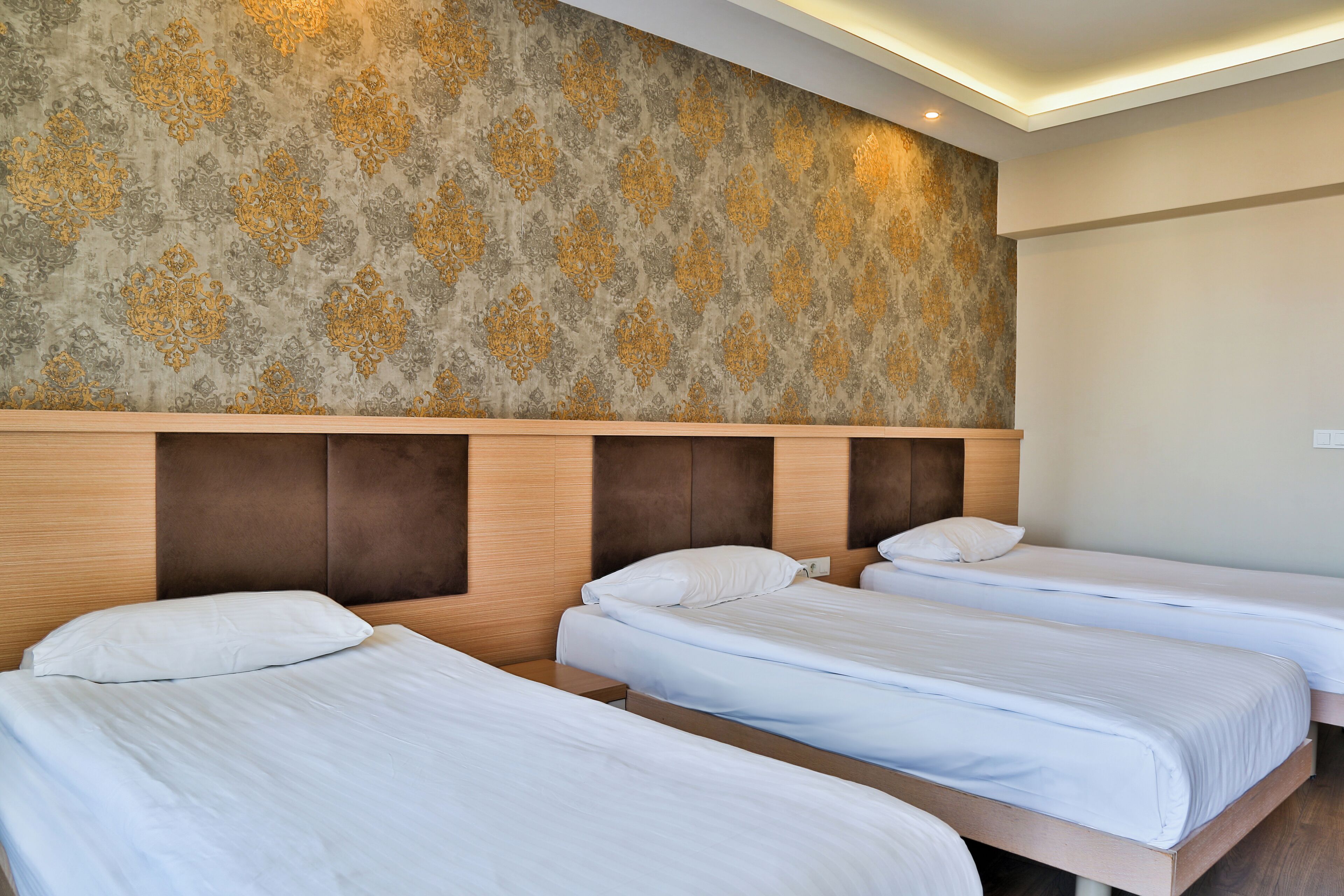 Ein Hotelzimmer mit drei Einzelbetten, einem hölzernen Kopfteil und einer Wand mit Muster.