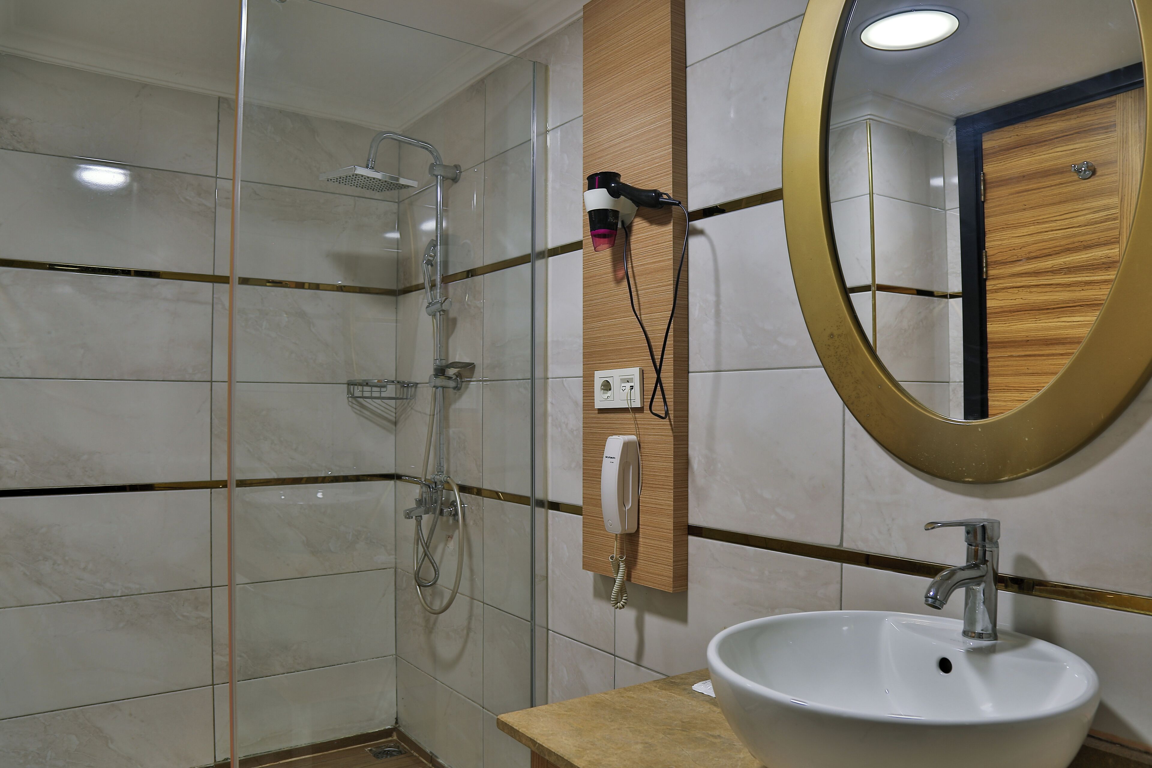 A bathroom with a shower, a sink, a mirror, and a hairdryer on the wall.