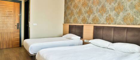 A hotel room with two single beds, a wooden door, and a patterned wallpaper.