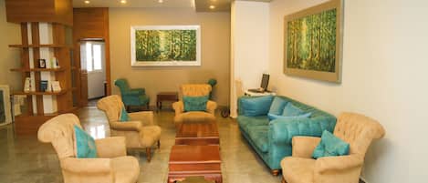 A spacious living area with a sofa, armchairs, and a coffee table. There are wooden shelves with books and decorative items.