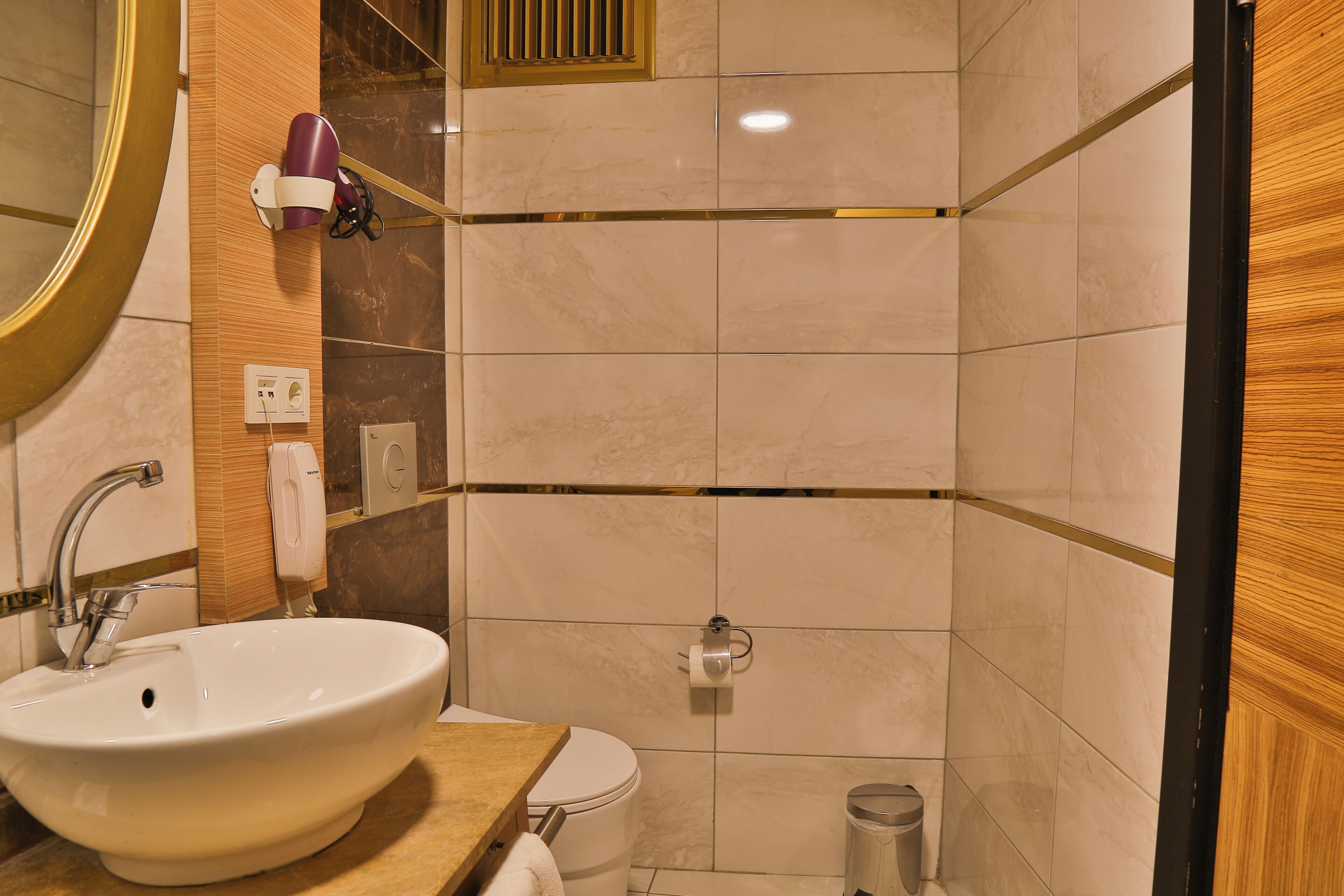 A bathroom with a sink, mirror, towel rack, toilet, and trash can.