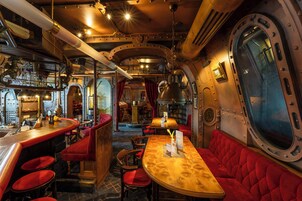 A bar area with red upholstered seating, a wooden bar counter, and a large window.