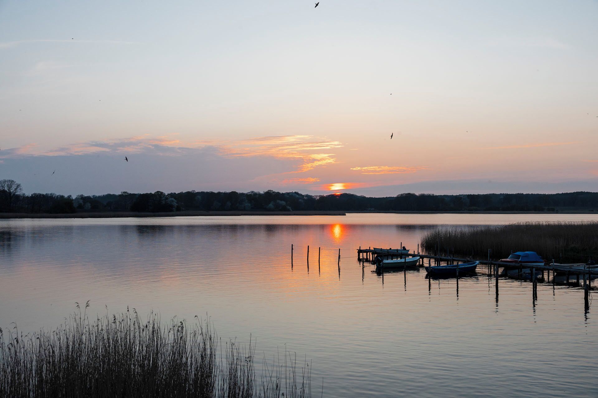 A calm lake at sunset with boats docked at the pier.