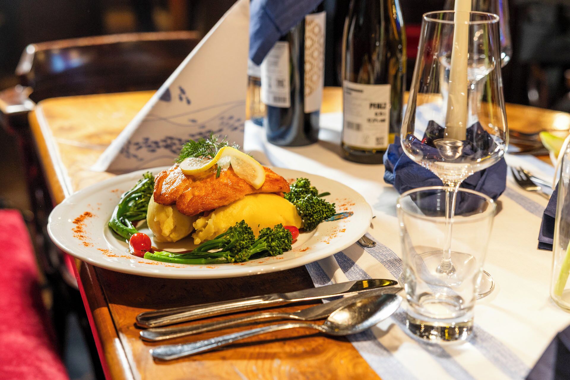 Una mesa de comedor con un plato de comida, un vaso de agua y botellas de vino.