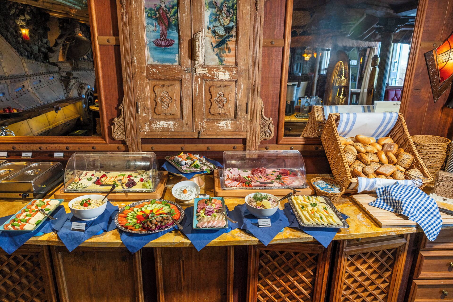 Un buffet proposant une variété de plats, notamment des salades, des viandes et des pains, dans un décor intérieur en bois agrémenté d’éléments décoratifs.