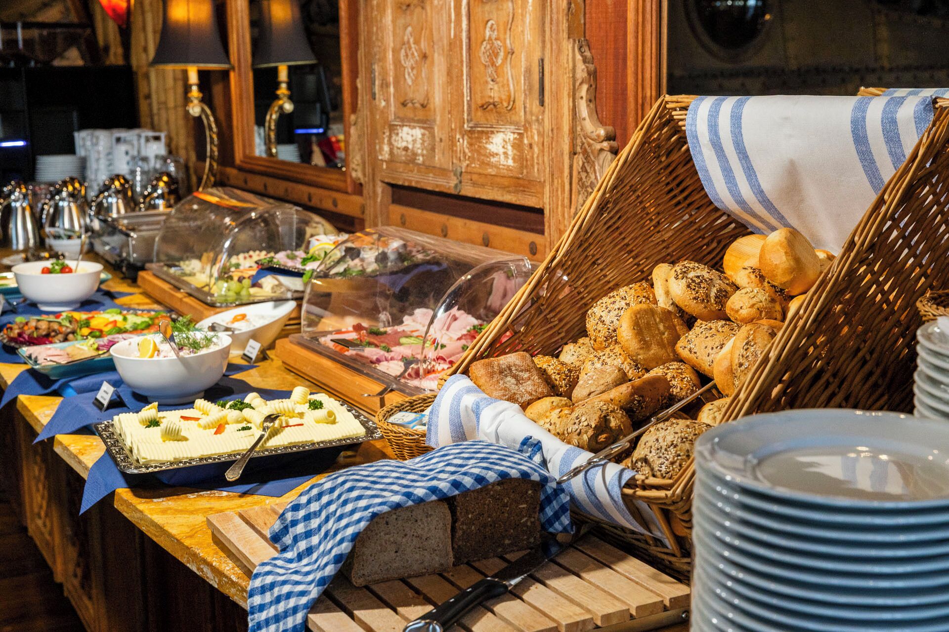 A buffet with various food items, including bread, pasta, and salads, displayed on a wooden table with a checkered cloth.