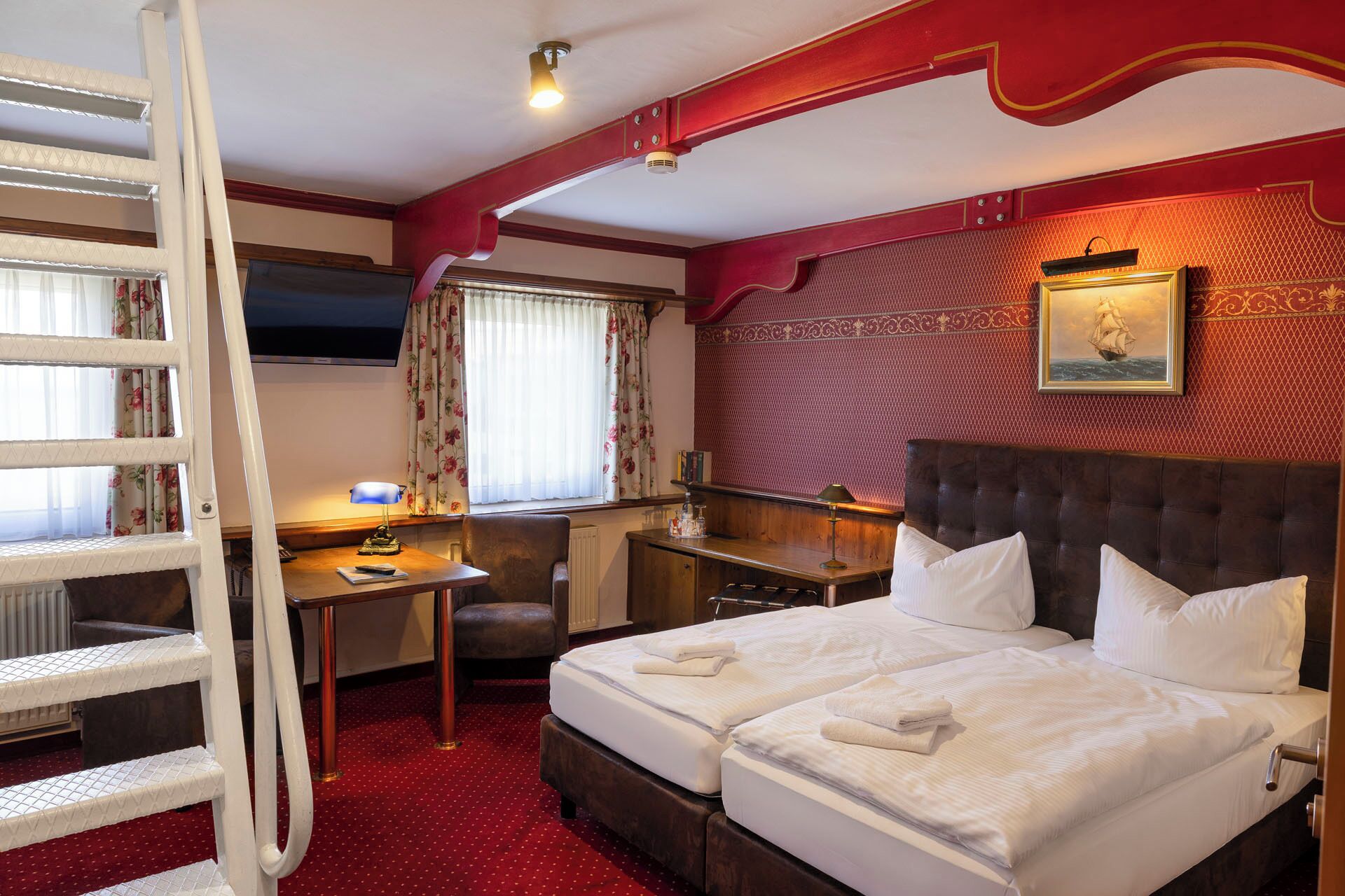 A hotel room with a bed, desk, chair, and a ladder.