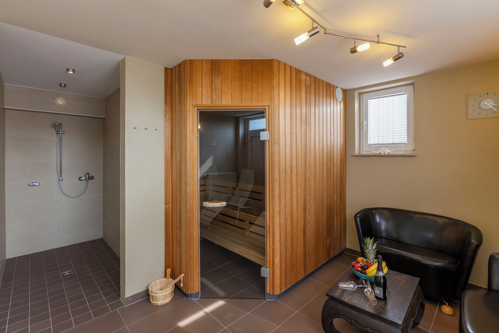 A modern bathroom with a shower, a wooden partition, and a seating area with a table and a bowl of fruit.