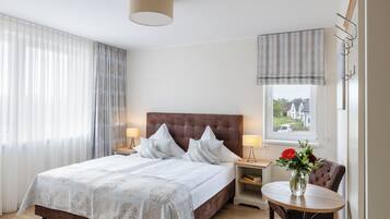 Ett hotellrum med en stor säng, två sänglampor, ett litet bord med en vas med blommor och utsikt över husen genom fönstret.