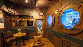 Una habitació amb decoració marina, que inclou una roda de vaixell, una taula rodona i una cadira bressol.