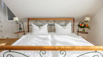 Een net opgemaakt bed met een houten hoofdbord en metalen frame, met aan beide zijden nachtkastjes, lampen en een bloevas.