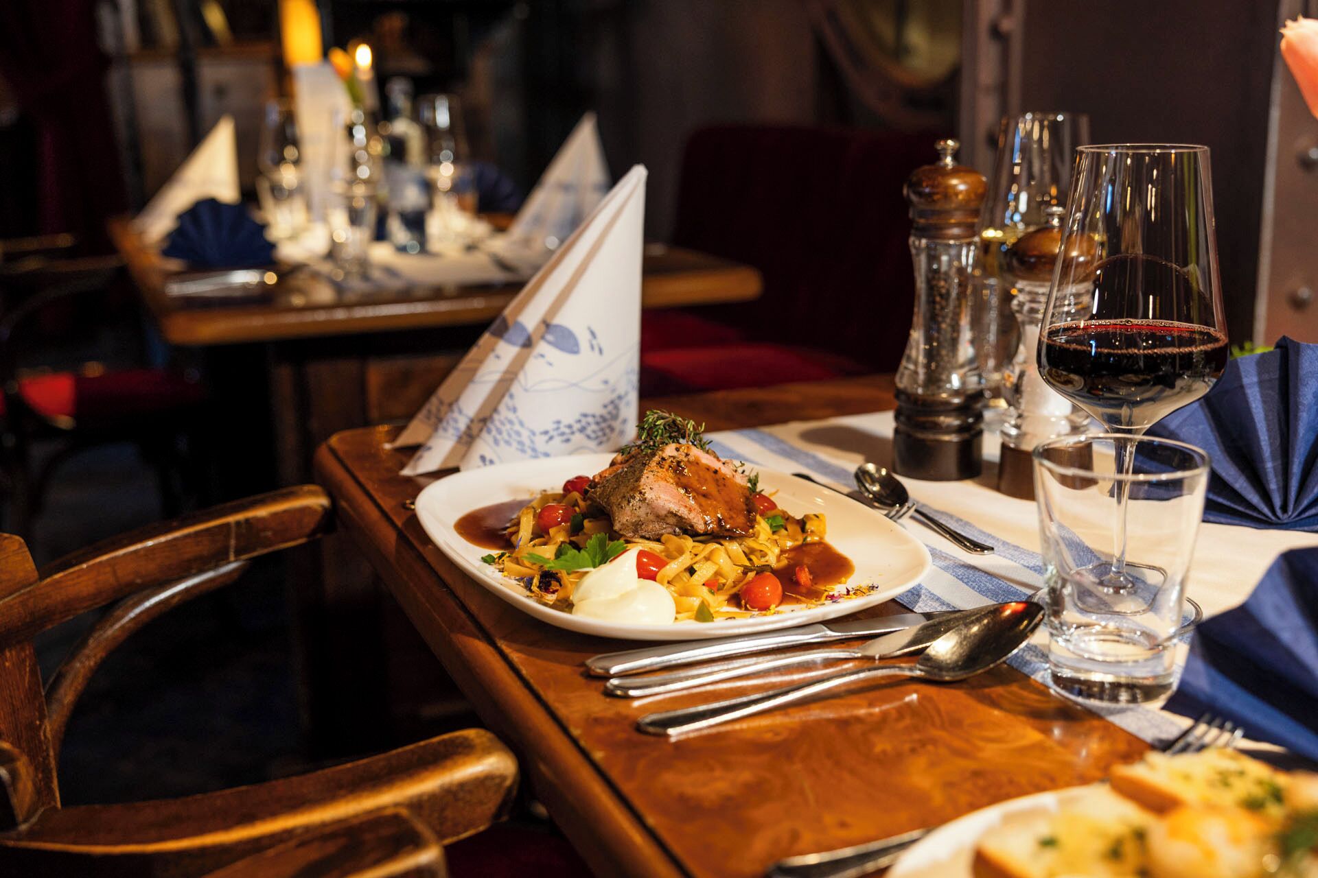 A dining table with a plate of food, cutlery, and a glass of red wine.