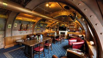 A ship's interior with a bar, seating, bookshelves, and a fireplace.